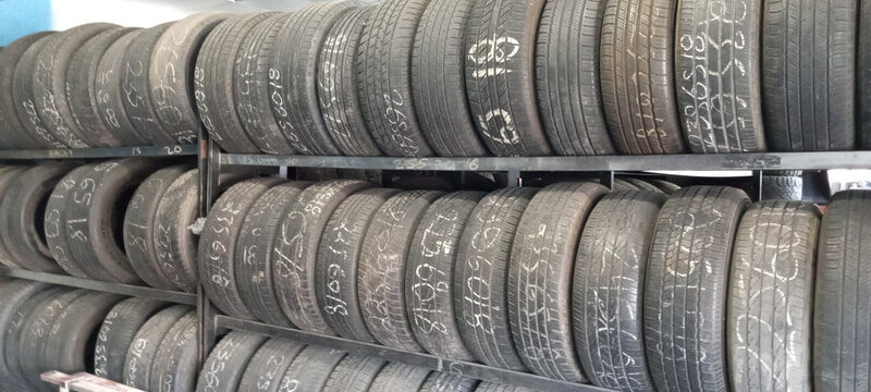Used tires on metal racks with chalk-written sizes and prices at Charleston Tires